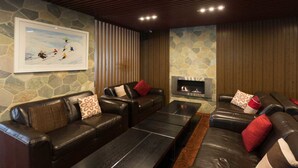 A modern living room with leather sofas, a fireplace, and a stone wall. - Duck Inn Mt Buller (Mount Buller)