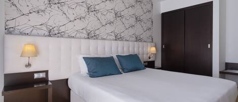 Un dormitorio con una cama grande, dos lámparas de noche, una mesita de noche de madera oscura y un armario oscuro.