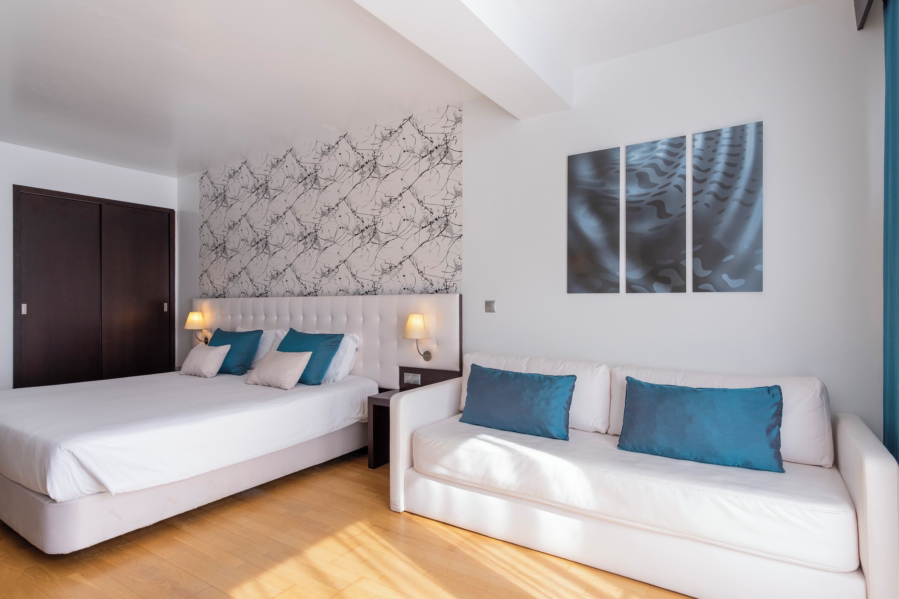 A hotel room with a large bed, a smaller bed, a sofa, and a wall with abstract art.