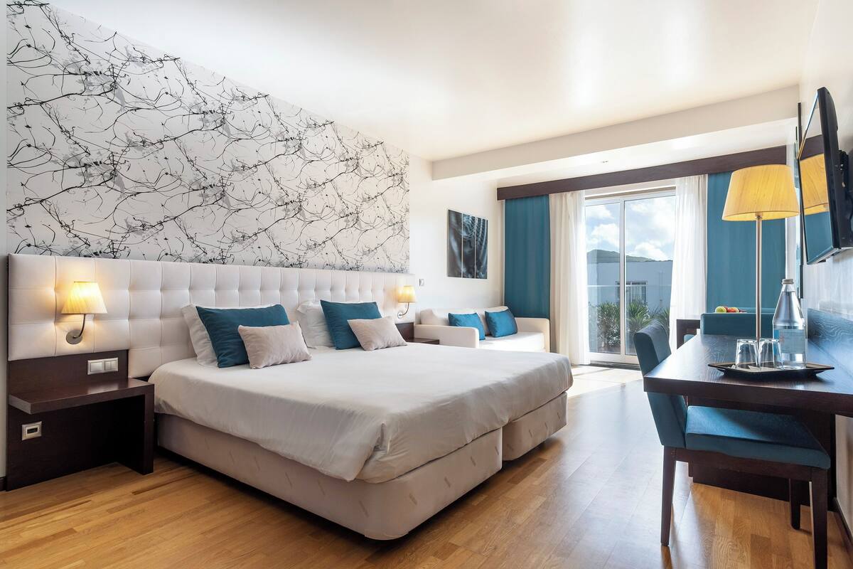 A modern hotel room with a large bed, a desk, and a view of the outdoors.
