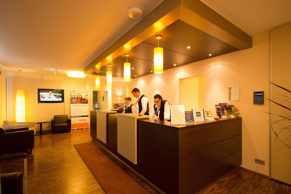 A hotel reception area with a reception desk, staff, and a television screen.