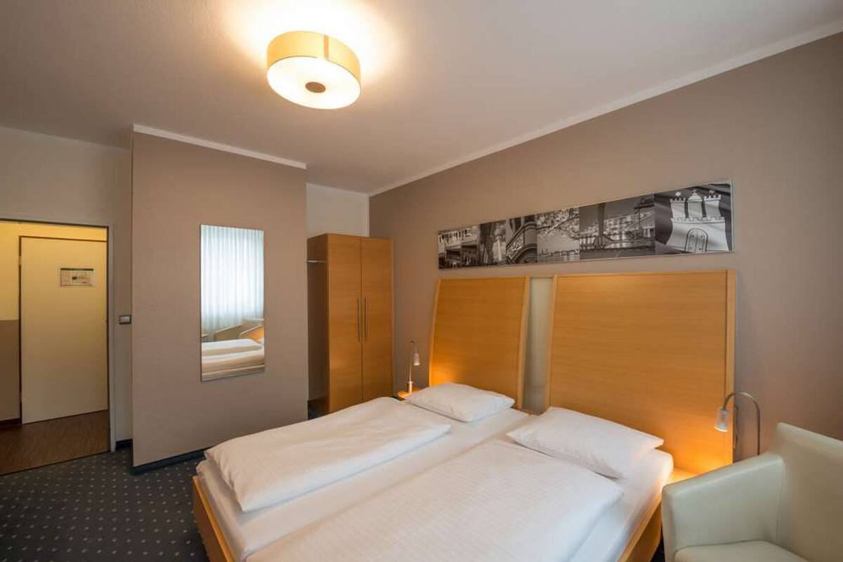 A hotel room with two beds, a large mirror, a wall-mounted artwork, and a ceiling light.