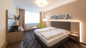 Habitació d'hotel amb llit, escriptori, cadira, làmpada i obra d'art a la paret.