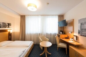 A hotel room with a bed, a desk, a chair, a TV, and a window with curtains. - Heikotel - Hotel Stadtpark Residenz (Hamburg)