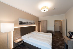 A hotel room with a large bed, bedside tables, a desk, a wardrobe, and a framed picture on the wall.