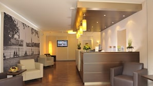 Rebedor d'hotel amb una taquilla de recepció, zona de seients i un gran quadre de paisatge urbà a la paret.