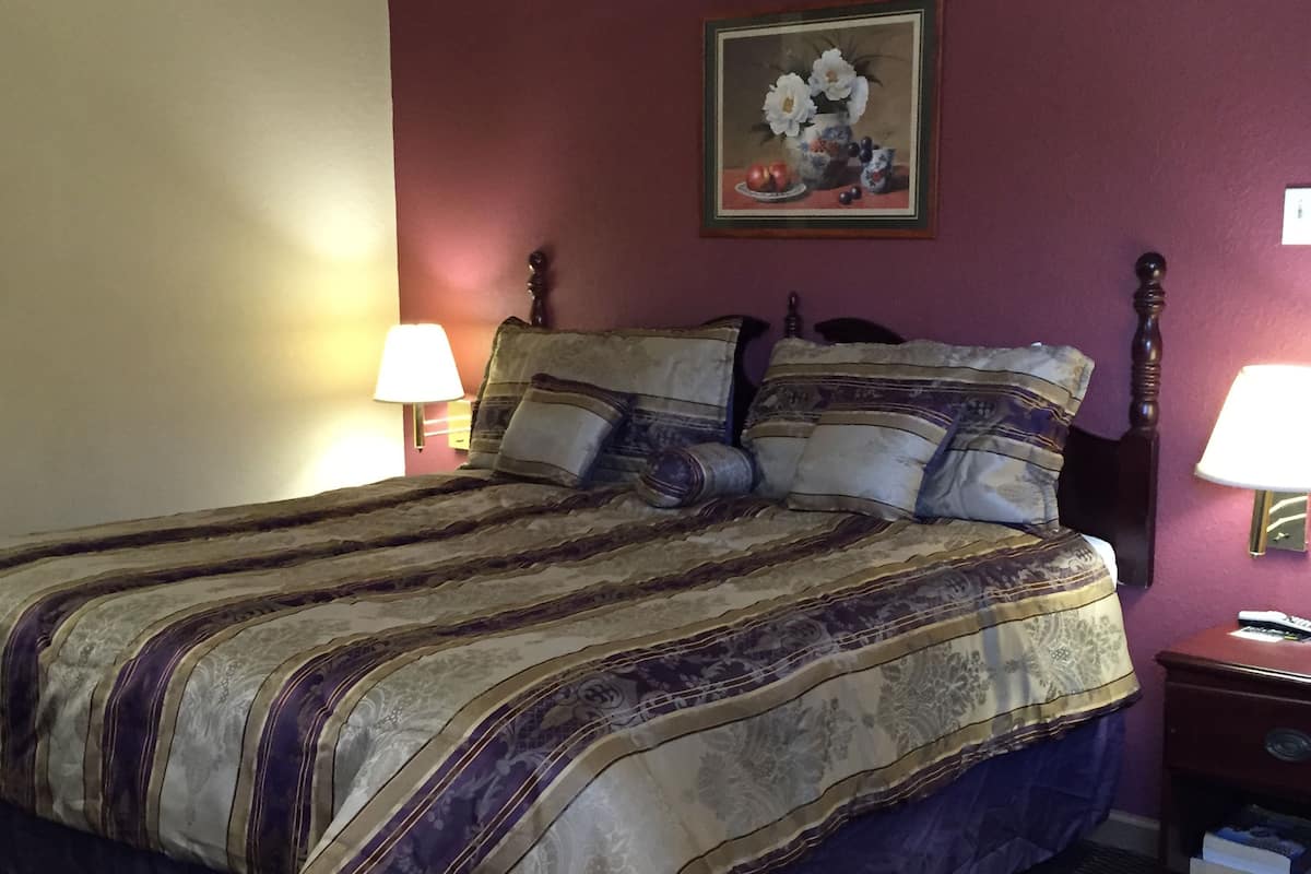 A neatly made bed with a patterned bedspread, two bedside lamps, a nightstand with a remote control, and a painting on the wall.