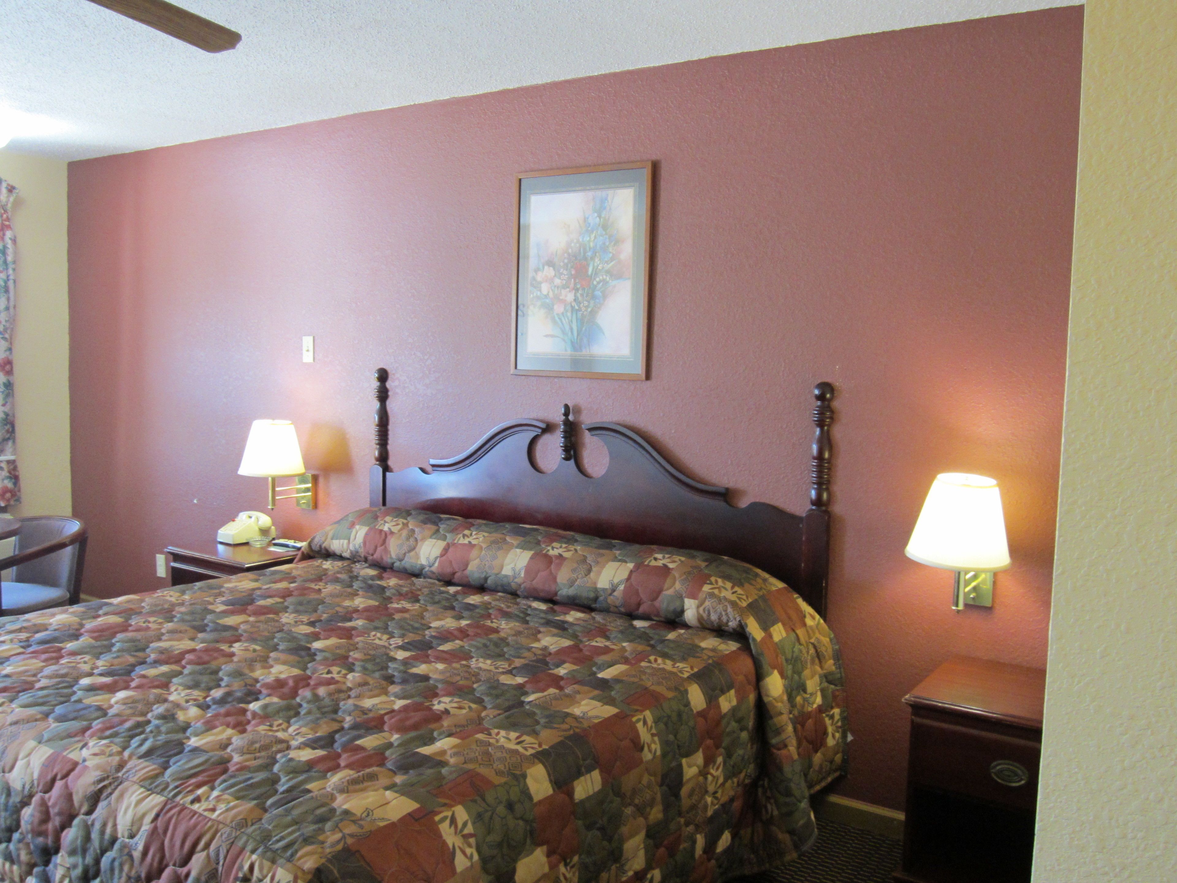 A neatly made bed with a floral quilt, a wooden headboard, and two bedside lamps.
