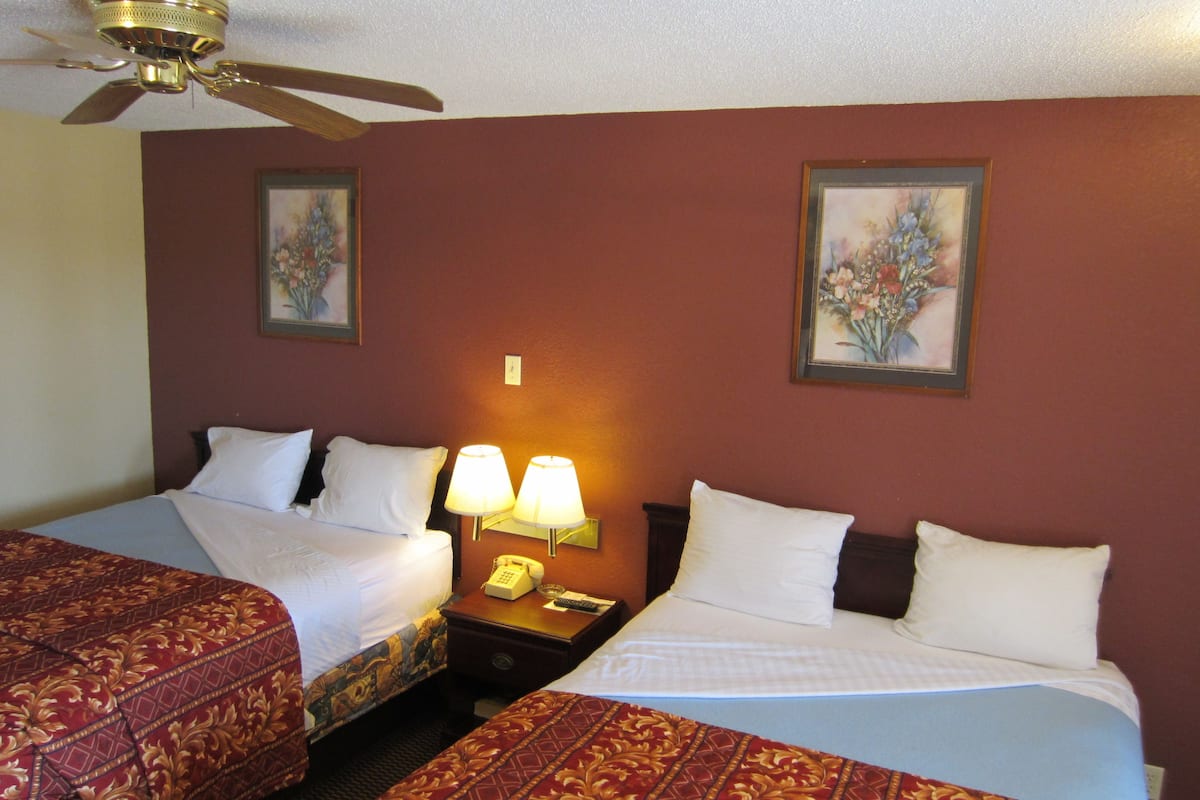 A hotel room with two beds, a ceiling fan, and two wall-mounted lamps.