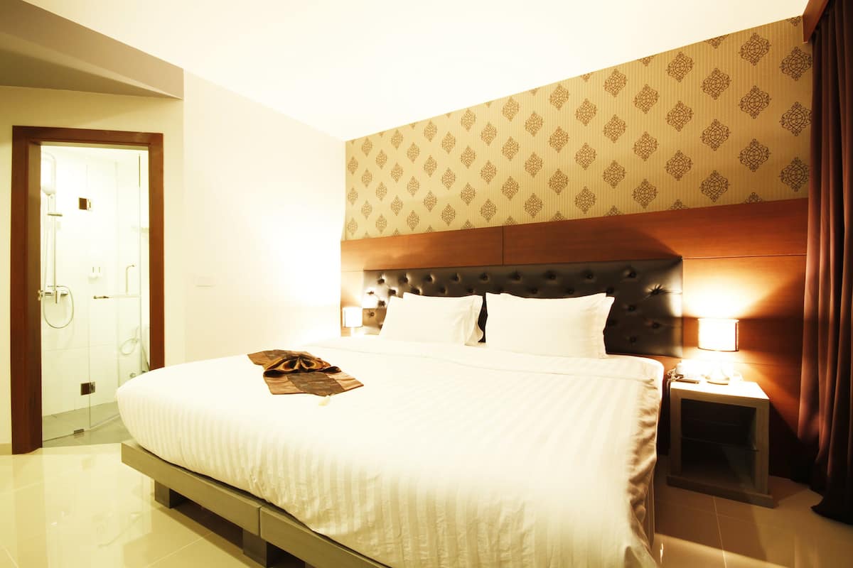 Une chambre d’hôtel avec un grand lit, une tête de lit en bois, une table de chevet avec une lampe et un papier peint à motifs.
