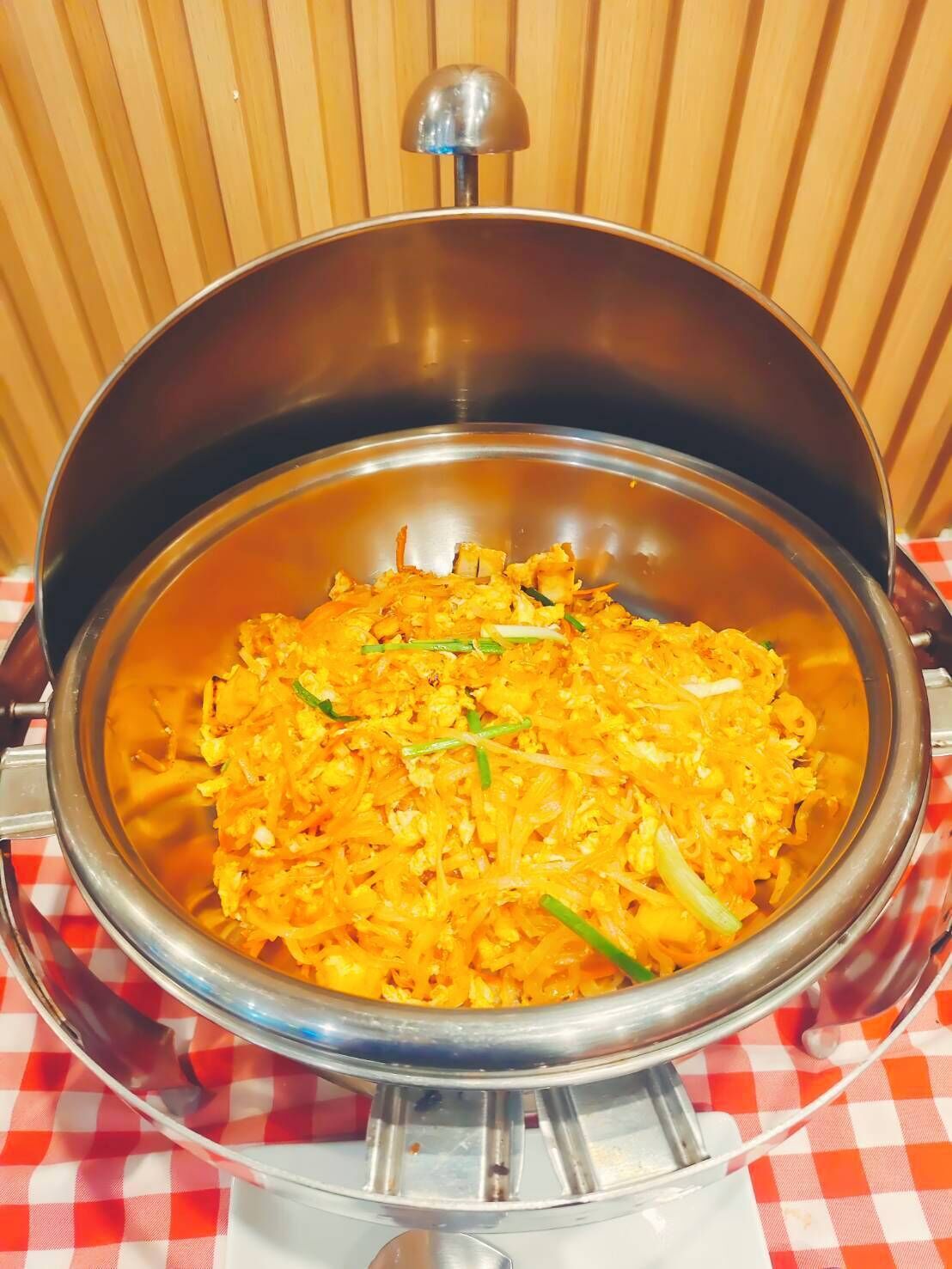 Un tazón metálico grande lleno de un plato de comida, sobre una mesa con mantel a cuadros.