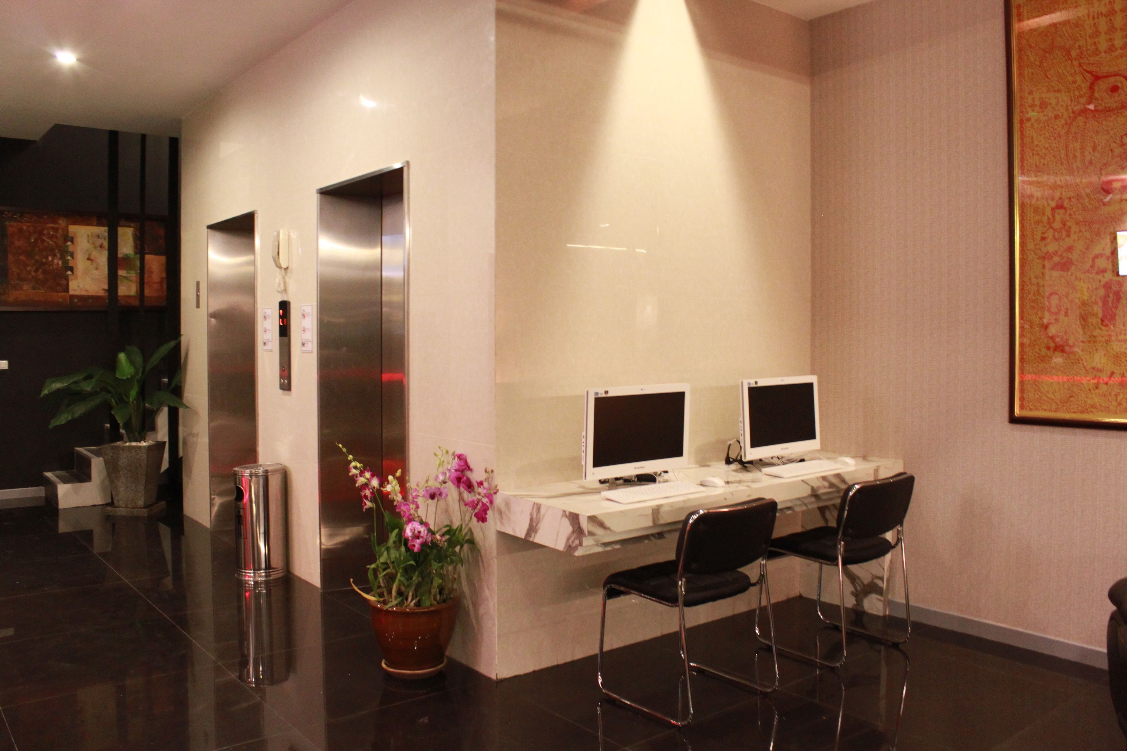 A reception area with two computer monitors, a desk, two chairs, a potted plant, and an elevator.