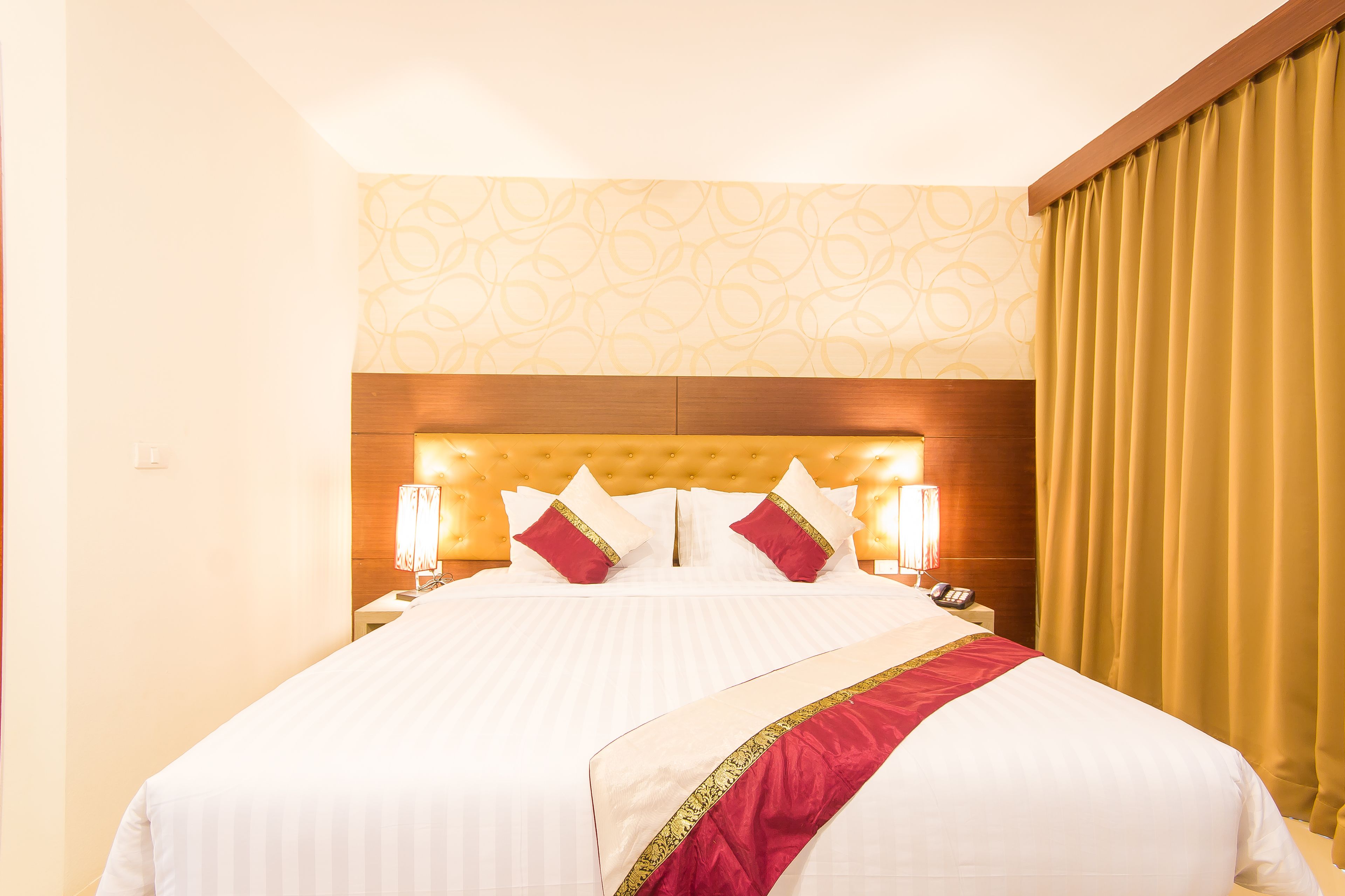 Habitación de hotel con una cama grande, dos mesitas de noche, una lámpara y una cortina.