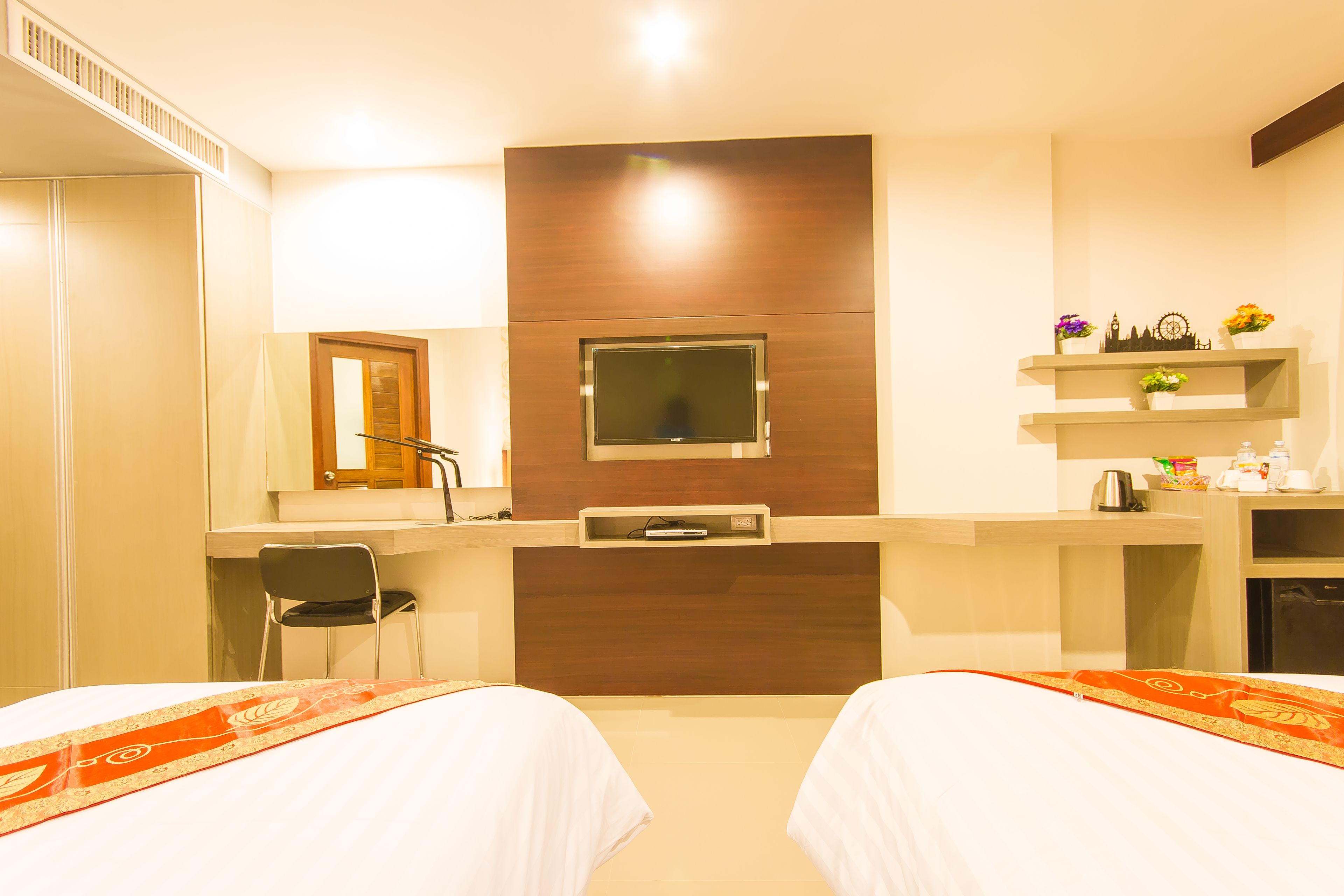 A hotel room with two beds, a desk, a chair, a TV, and a small kitchenette.