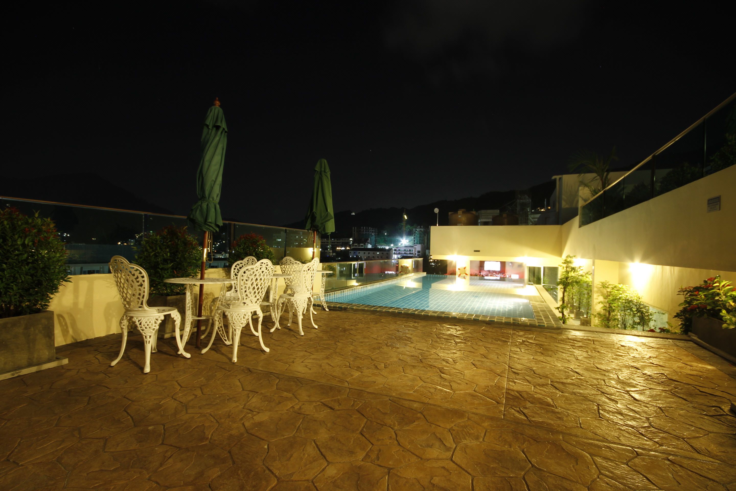 An outdoor pool area with white chairs and umbrellas, a tiled floor, and a building in the background.