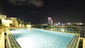 Una piscina infinita en la azotea con vistas a la ciudad de noche.