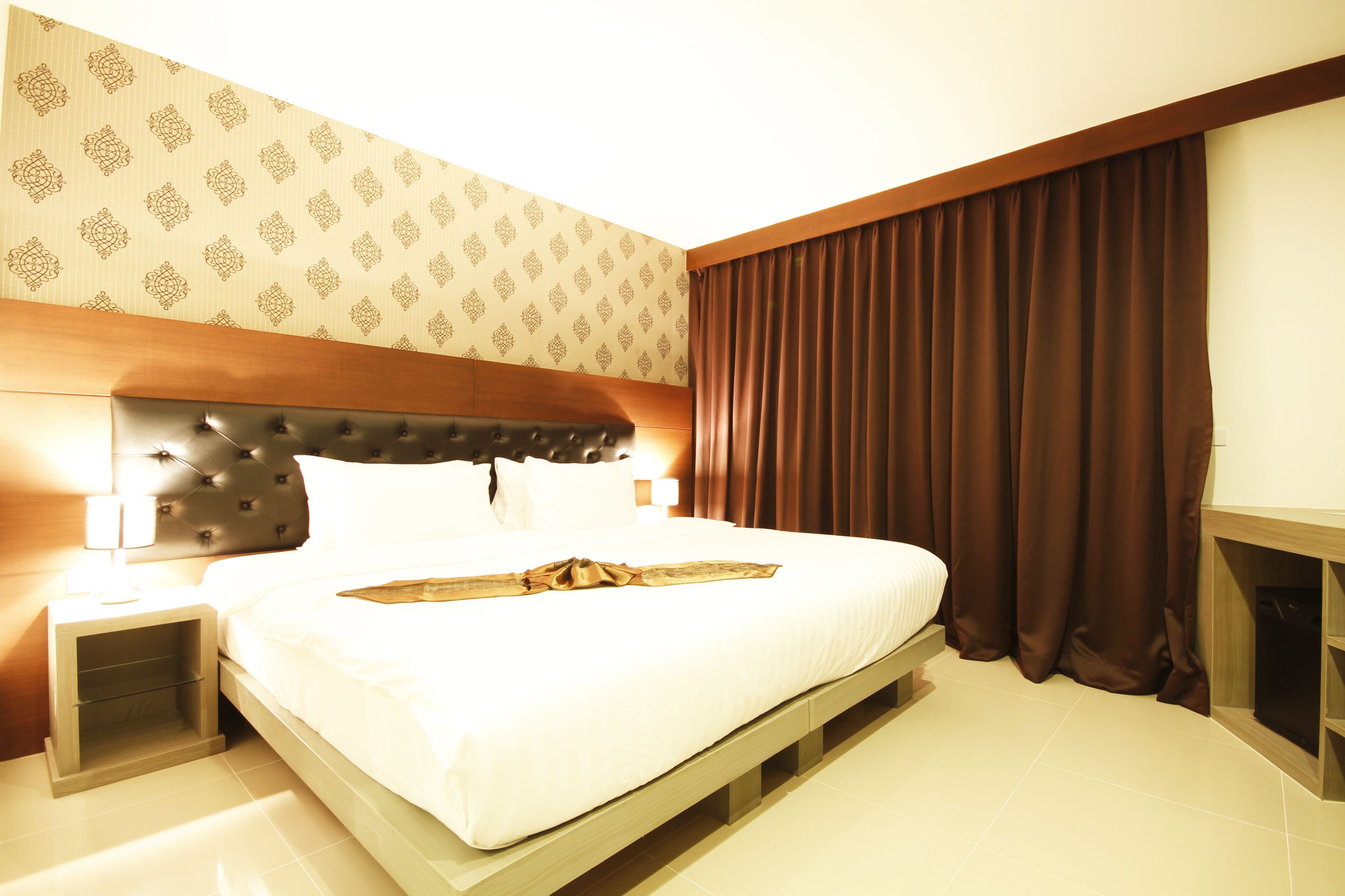 A hotel room with a large bed, a headboard, a nightstand, a bedside table, and a curtain.