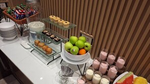 Un bufé con una variedad de alimentos, como muffins, pasteles, frutas y bebidas.