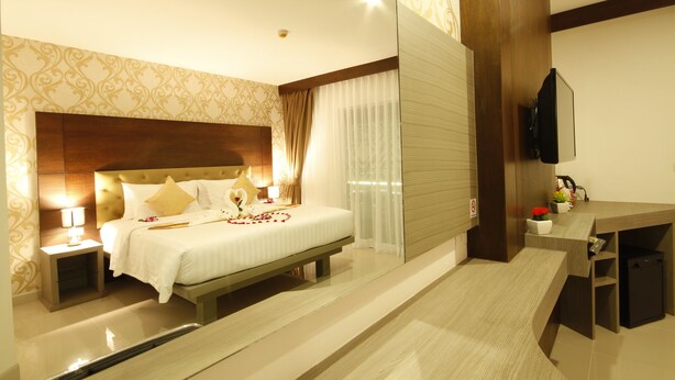 Una habitación de hotel con una cama grande, mesitas de noche, un escritorio y un espejo.