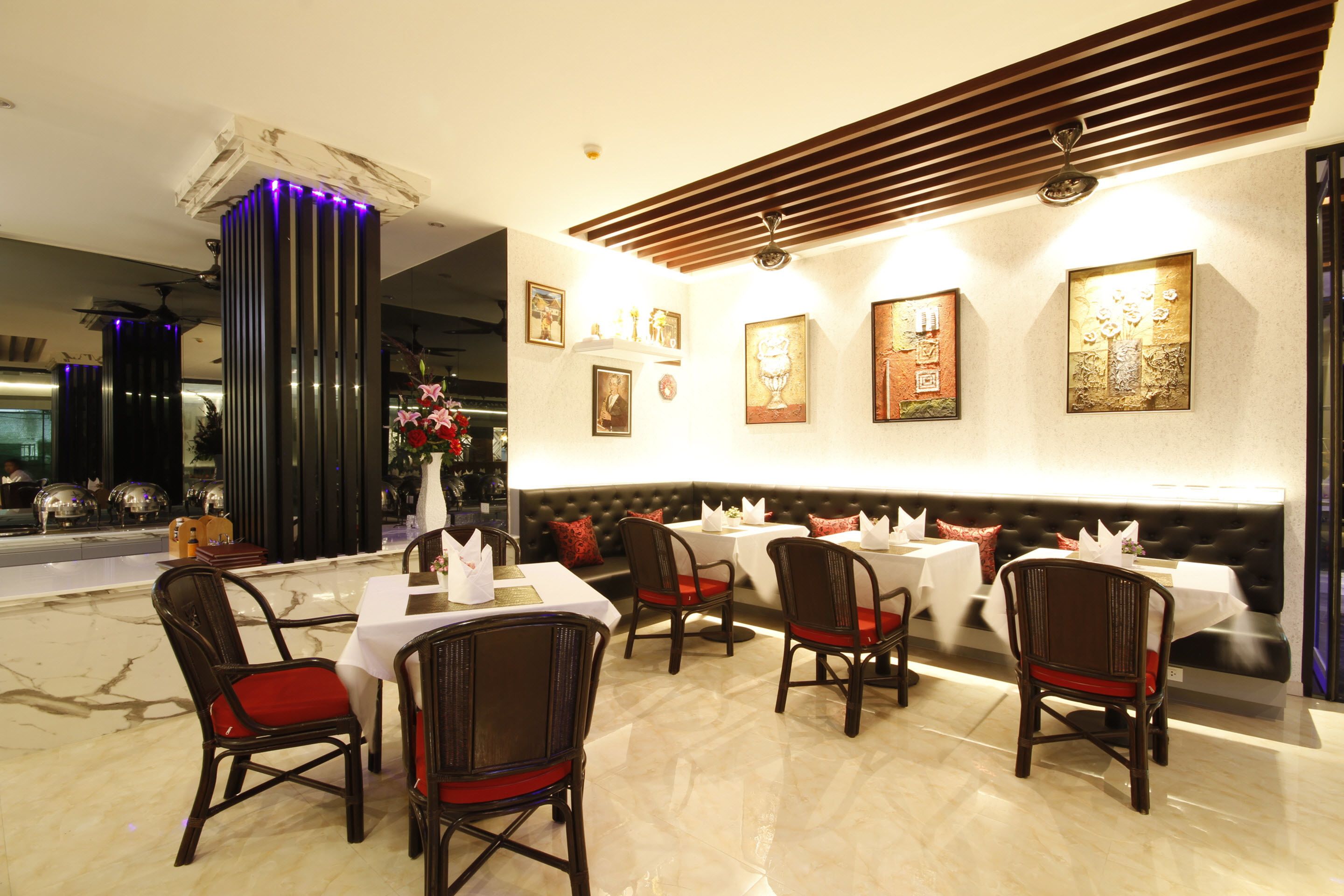 A restaurant with marble flooring, dark wooden chairs with red cushions, white tablecloths, and framed artwork on the walls.