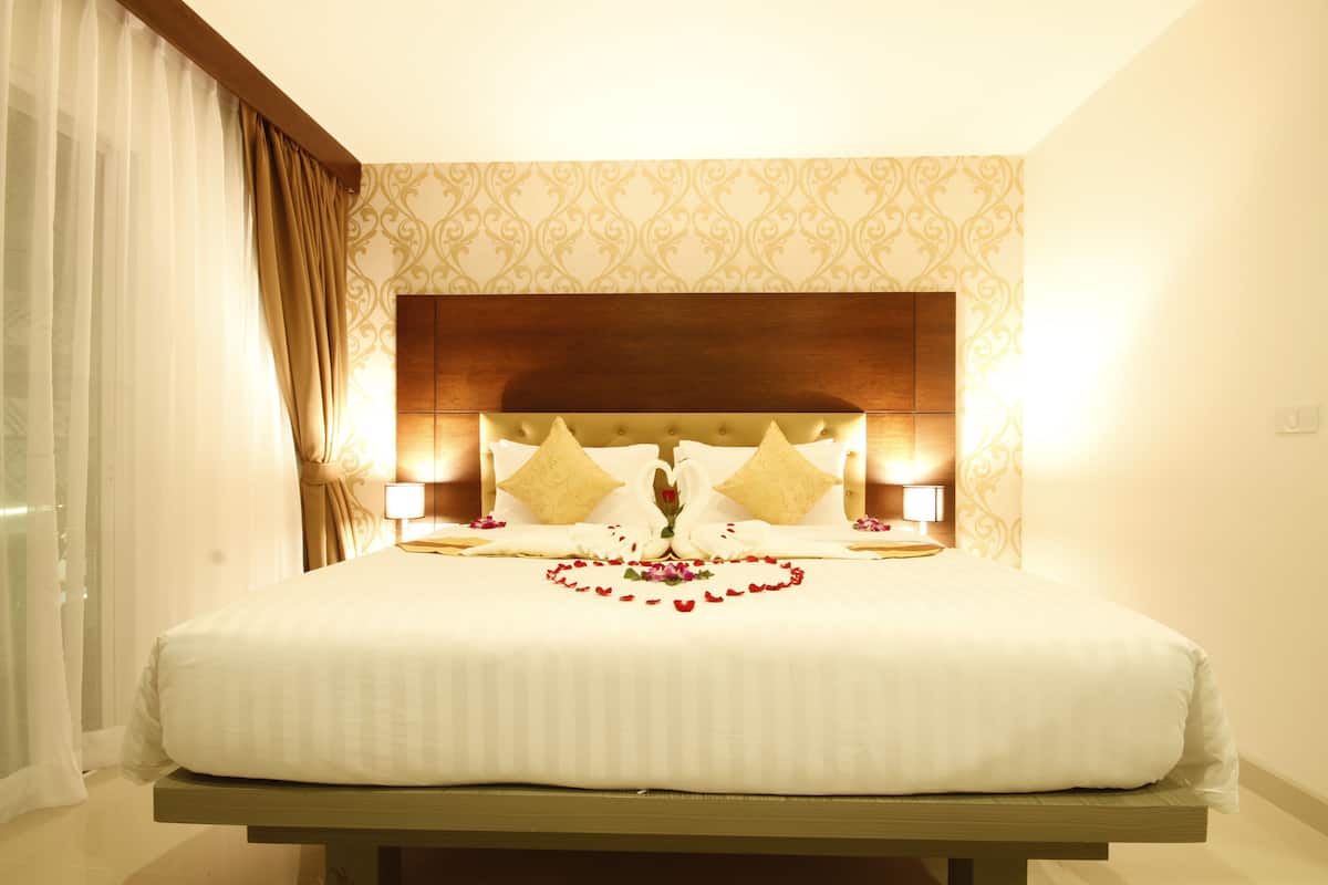 Un lit bien fait, agrémenté d’un arrangement floral en forme de cœur, de deux coussins décoratifs et de lampes de chevet.