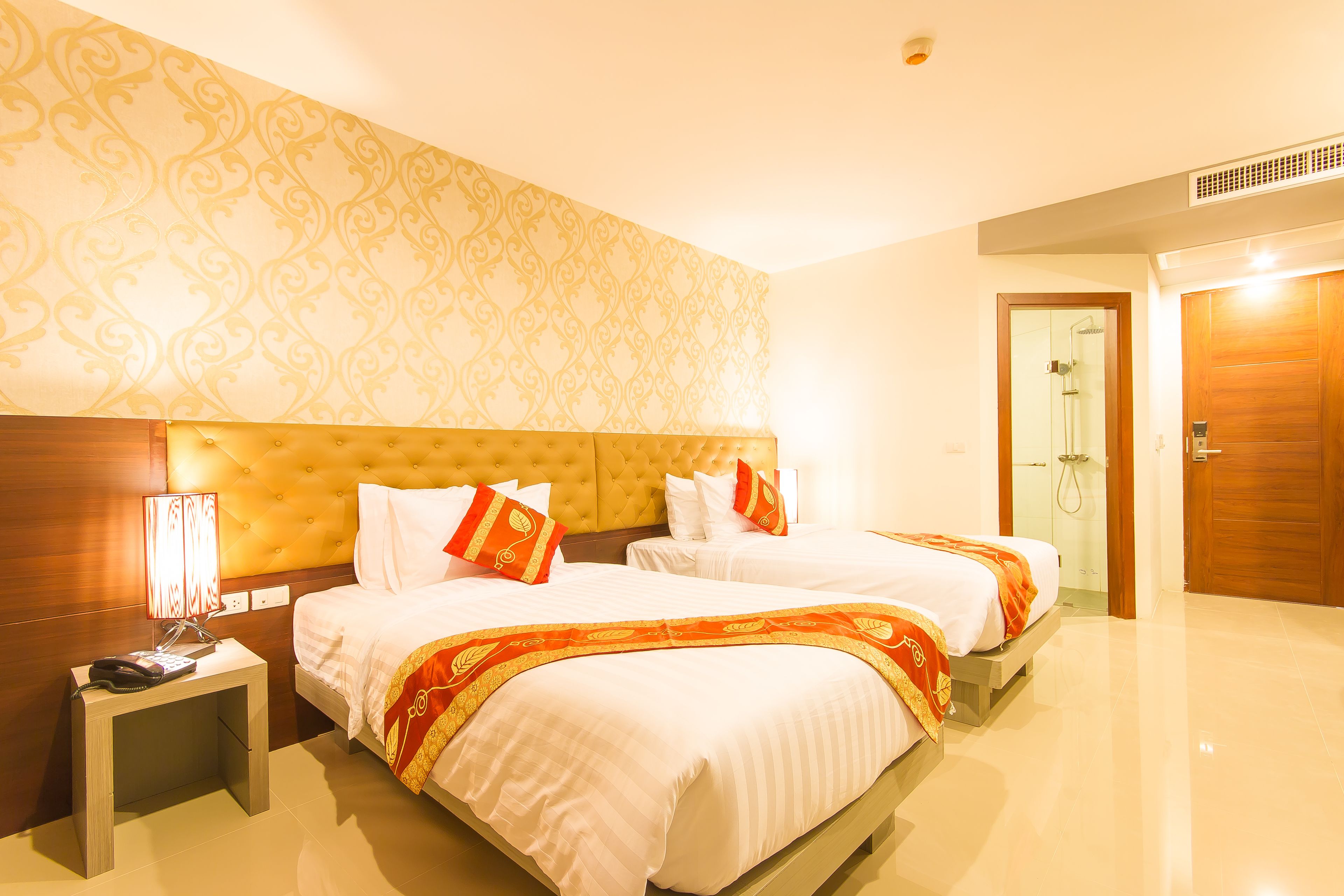 A hotel room with two beds, a wooden headboard, a nightstand with a lamp, and a shower area.
