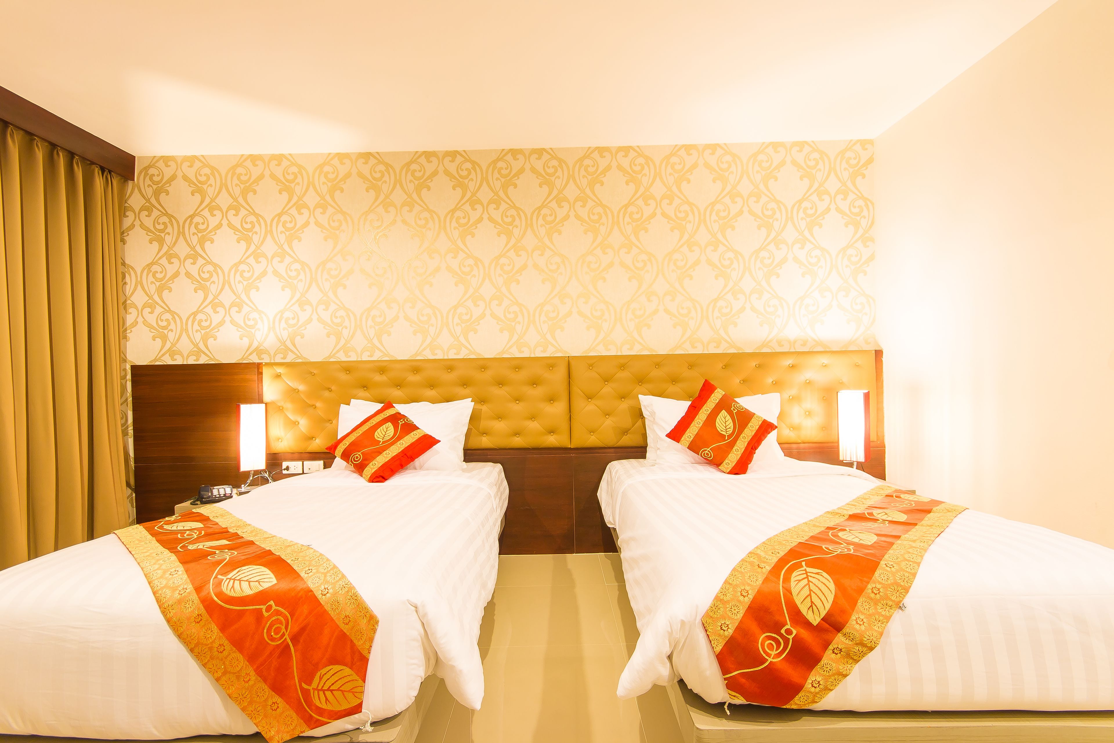 A hotel room with two beds, a tufted headboard, and patterned wallpaper.