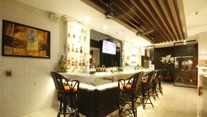 Zona de bar con mostrador de mármol, varios taburetes y una pantalla de televisión.