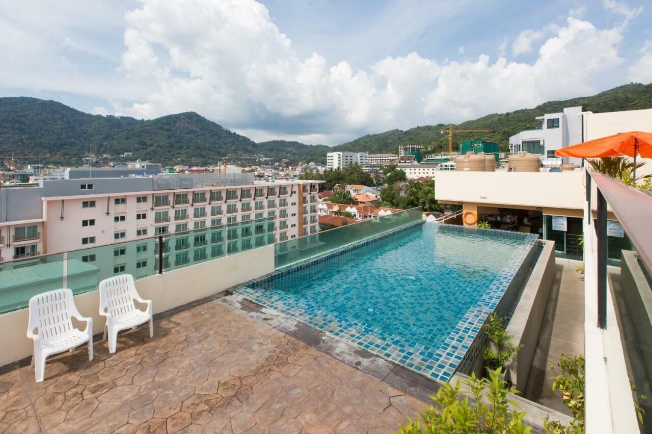 Una piscina en la azotea con agua cristalina, rodeada por una terraza de piedra y sillas blancas.