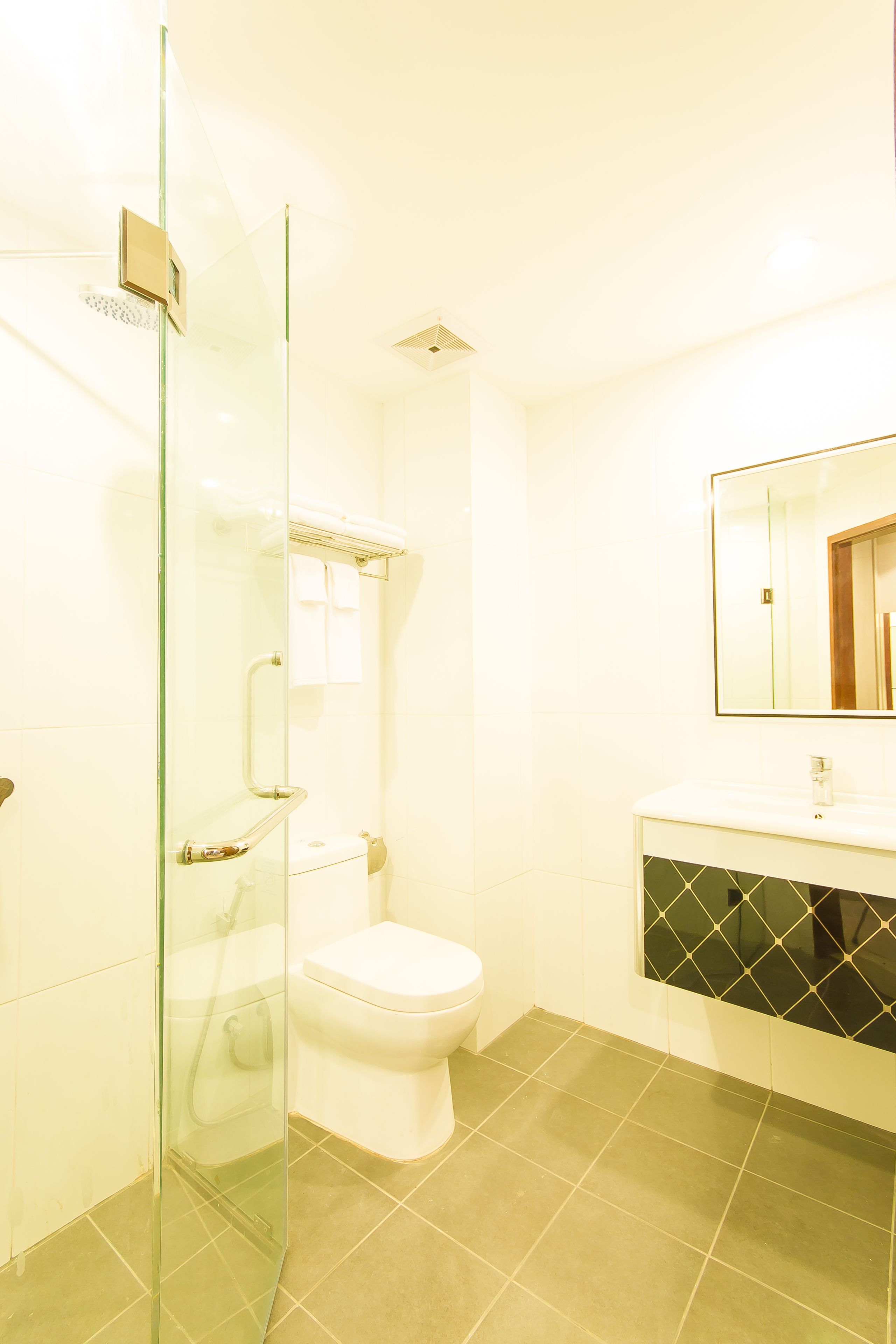 A modern bathroom with a glass shower enclosure, a white toilet, and a vanity with a black tiled backsplash.