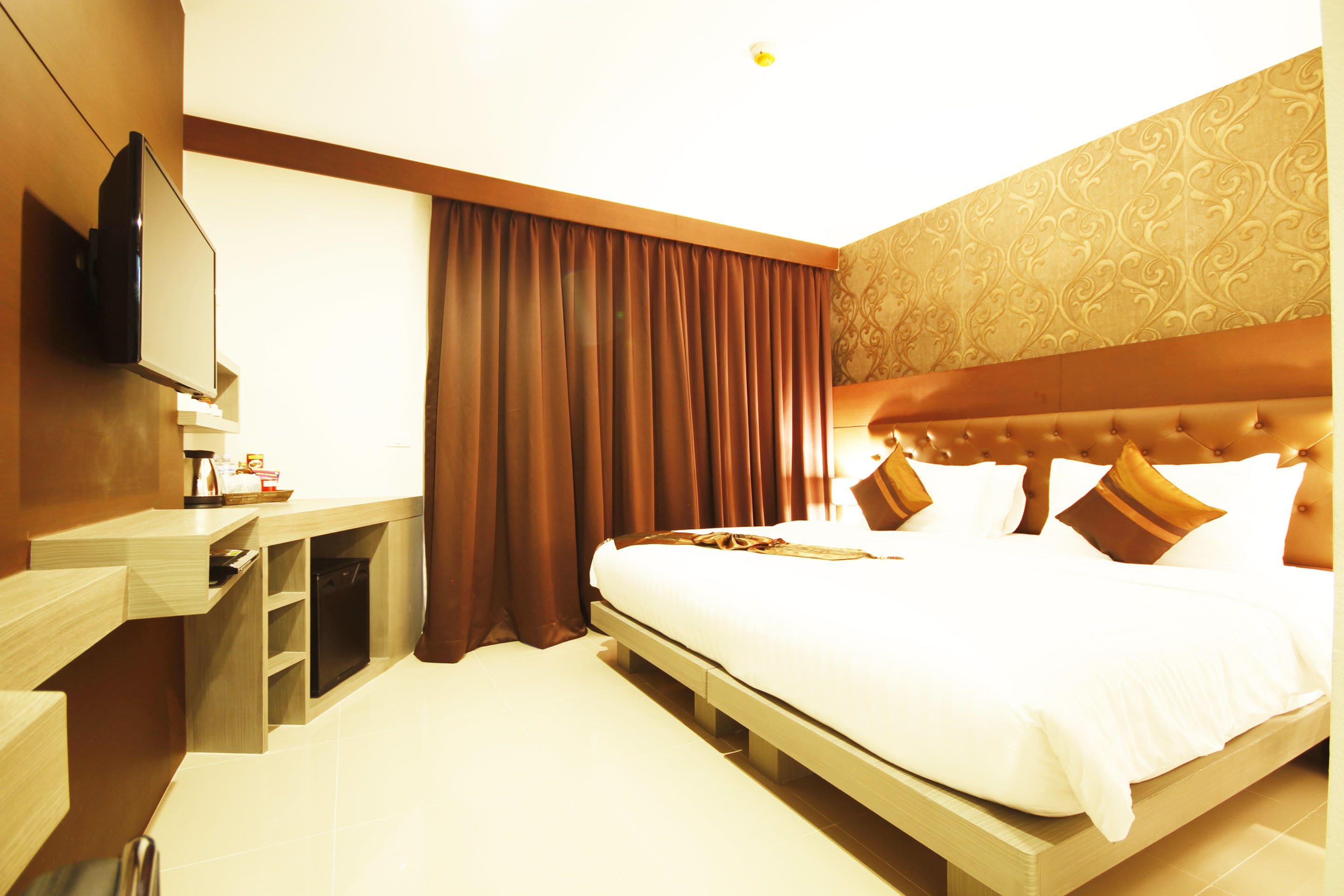 Habitación de hotel con cama, televisión de pantalla plana en la pared, escritorio pequeño con silla y ventana grande con cortinas.