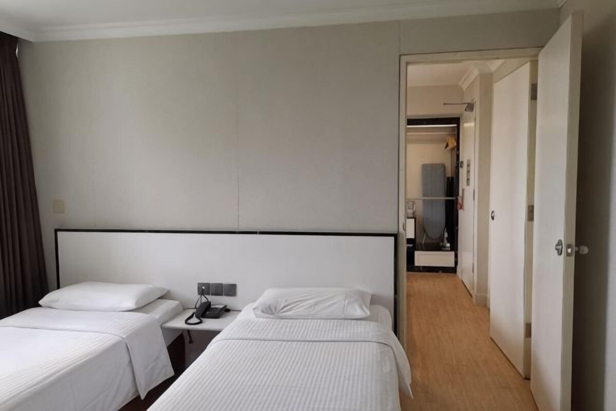 A hotel room with two single beds, a bedside table with a phone, and a door leading to a hallway.