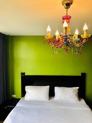Una cama con sábanas blancas, cabecera negra y pared verde.