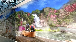 Una habitación con piso de madera, un mural grande de una cascada y un bosque, y una bañera de madera con dos perros.