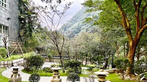 Un jardín con faroles de piedra, un puente de piedra y un edificio con tejado de baldosas.