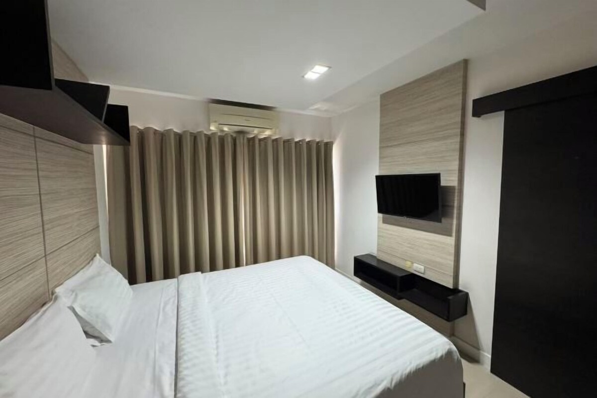 Una habitación de hotel moderna con una cama, un televisor de pantalla plana montado en la pared y un equipo de aire acondicionado integrado.