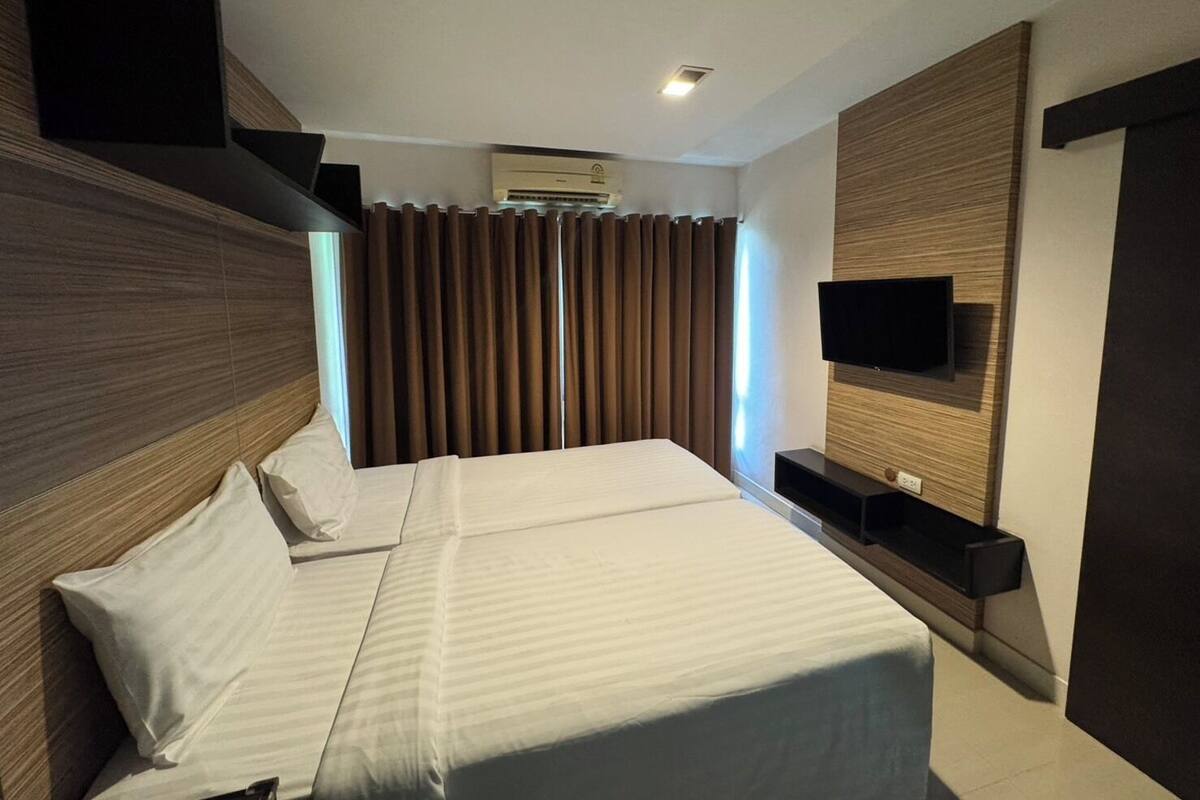 A modern hotel room with a large bed, a flat-screen TV mounted on the wall, and a built-in air conditioning unit.