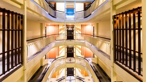 Un atrio de varios niveles con una escalera central, barandillas de vidrio y tragaluces.