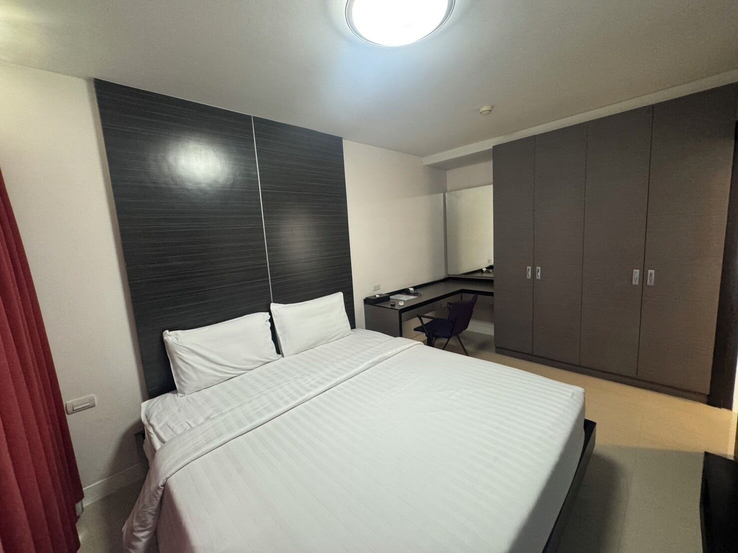 A modern hotel room with a large bed, a desk, and a wardrobe.