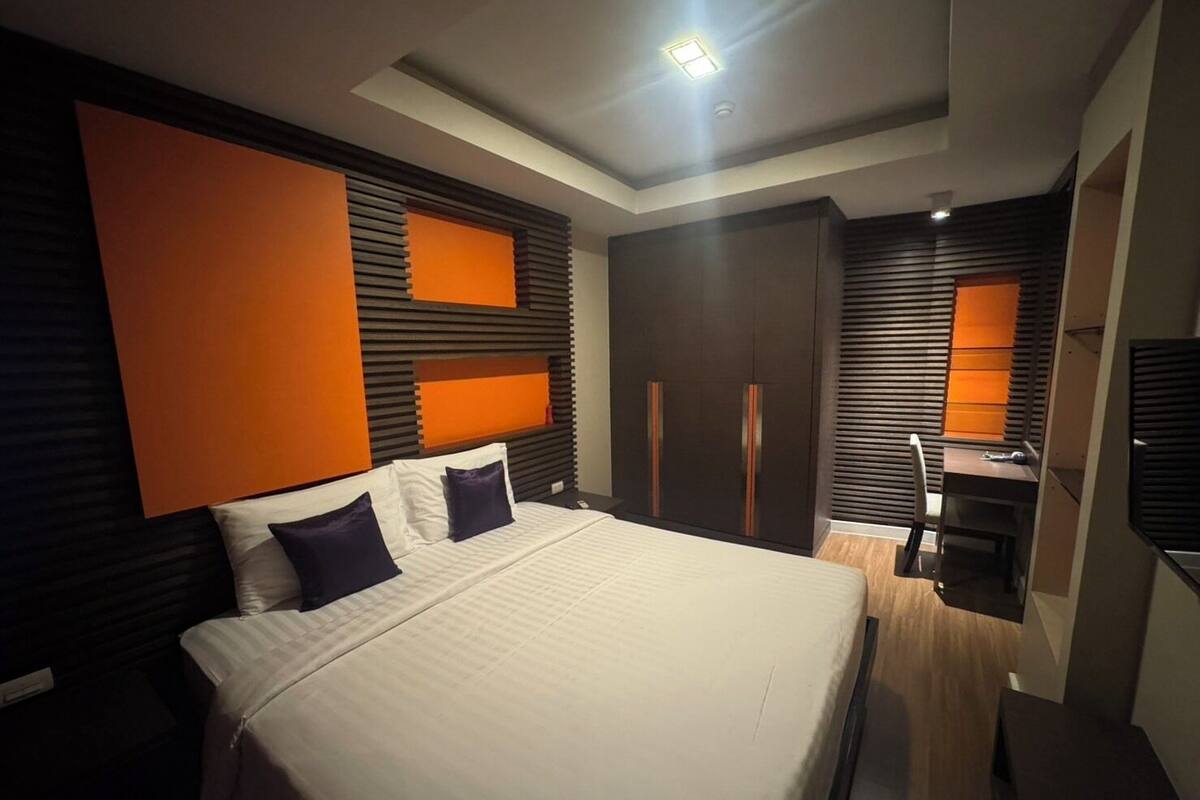 A modern bedroom with a large bed, a desk, and a wardrobe.