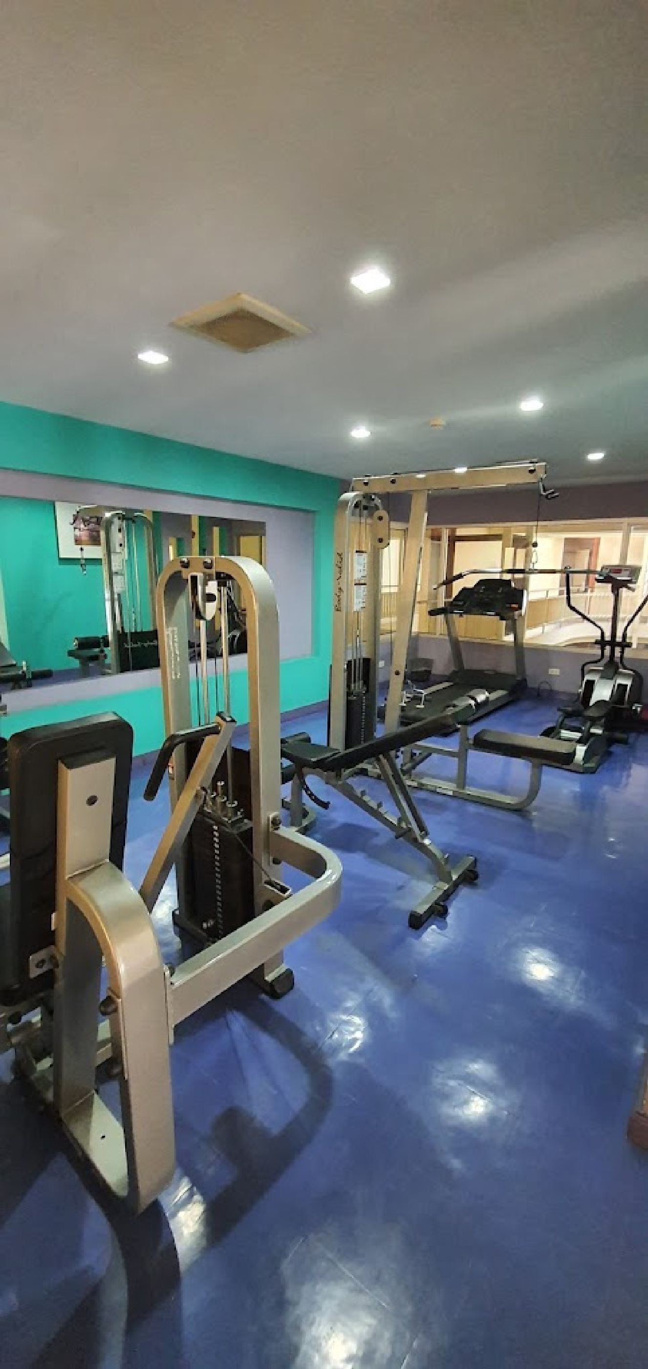 A gym with various exercise machines, a blue floor, and teal walls.