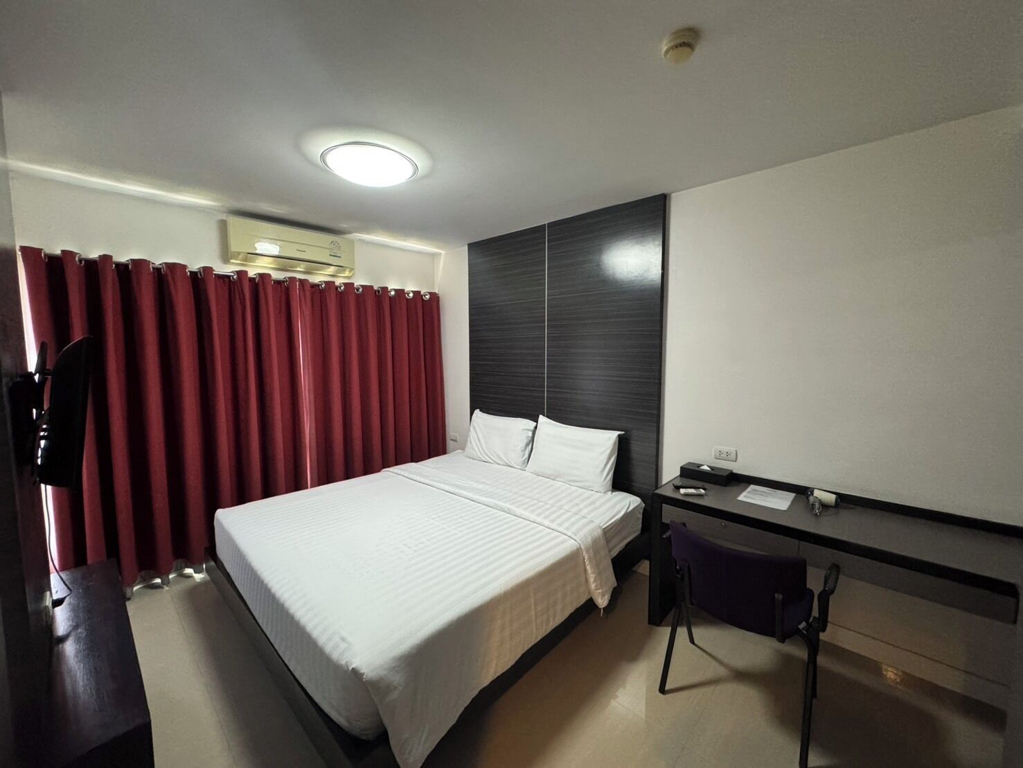 A hotel room with a bed, a desk, a chair, and a large mirror.