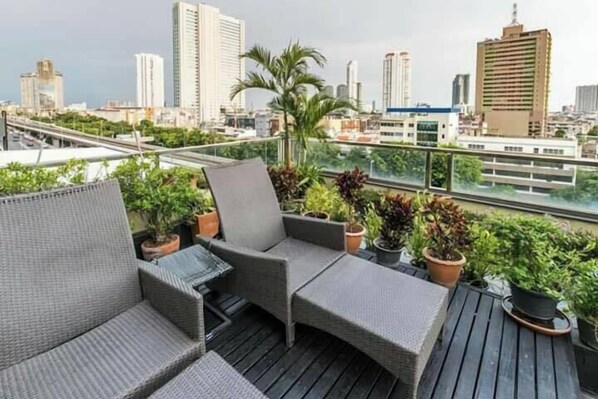 A rooftop terrace with wicker furniture, potted plants, and a city skyline view.