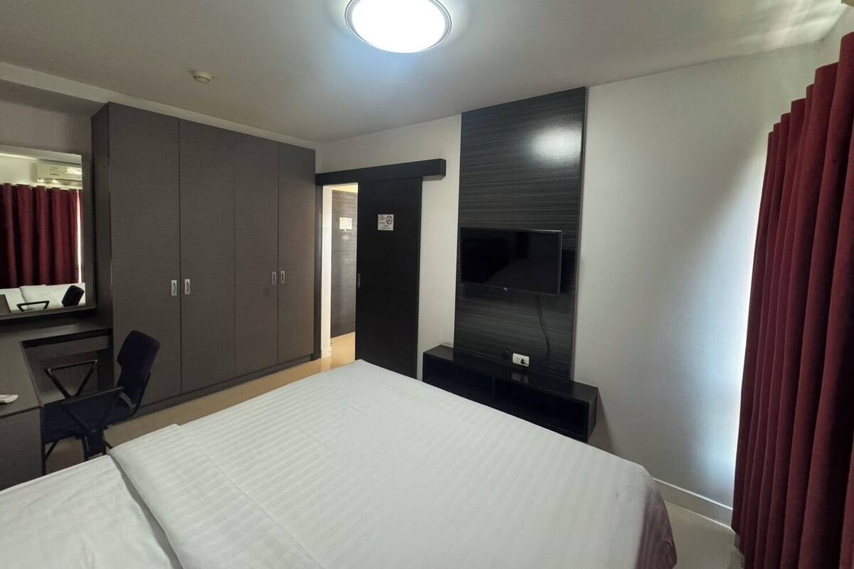 A hotel room with a bed, a desk, a chair, a wardrobe, and a TV mounted on the wall.