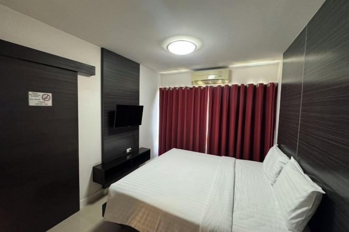 Una habitación de hotel con cama, televisor, armario oscuro y cortina roja.