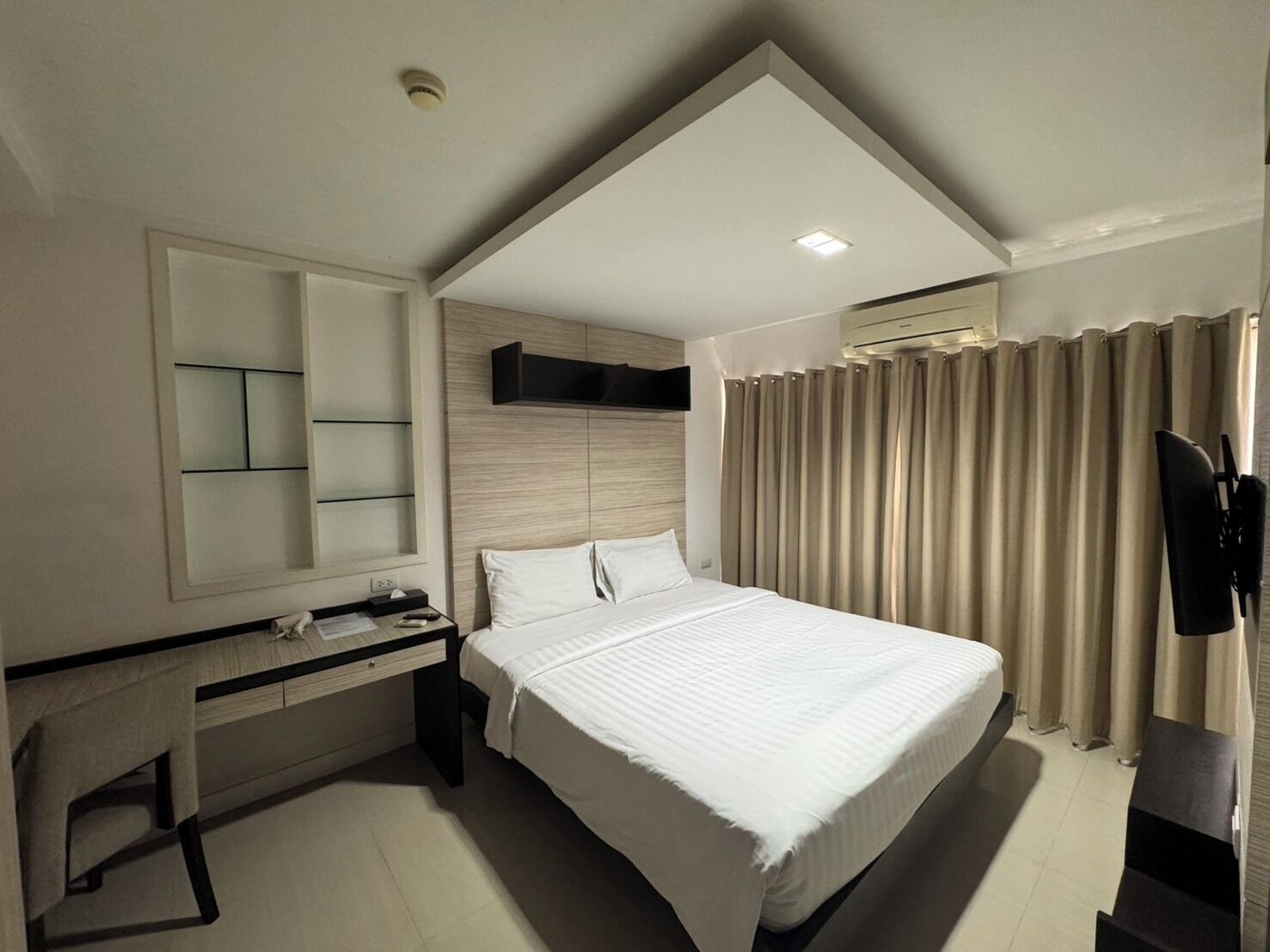 A modern hotel room with a bed, a desk, a mirror, and a TV.