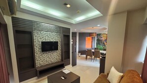 Una sala moderna con un televisor de pantalla plana, una pared con diseño de piedra, un comedor con mesa y sillas, y un sofá marrón.