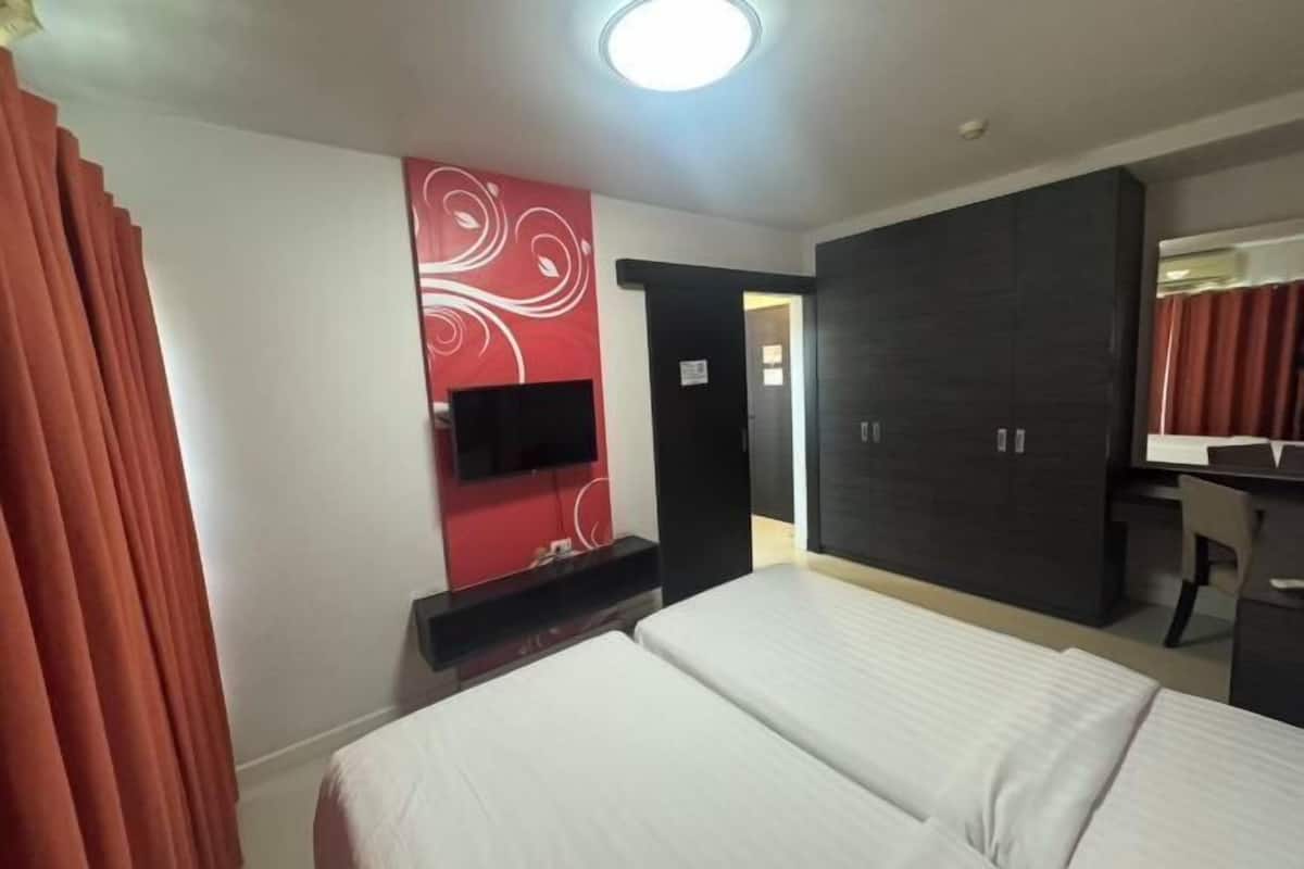 A hotel room with a bed, a TV mounted on the wall, a wardrobe, and a desk.
