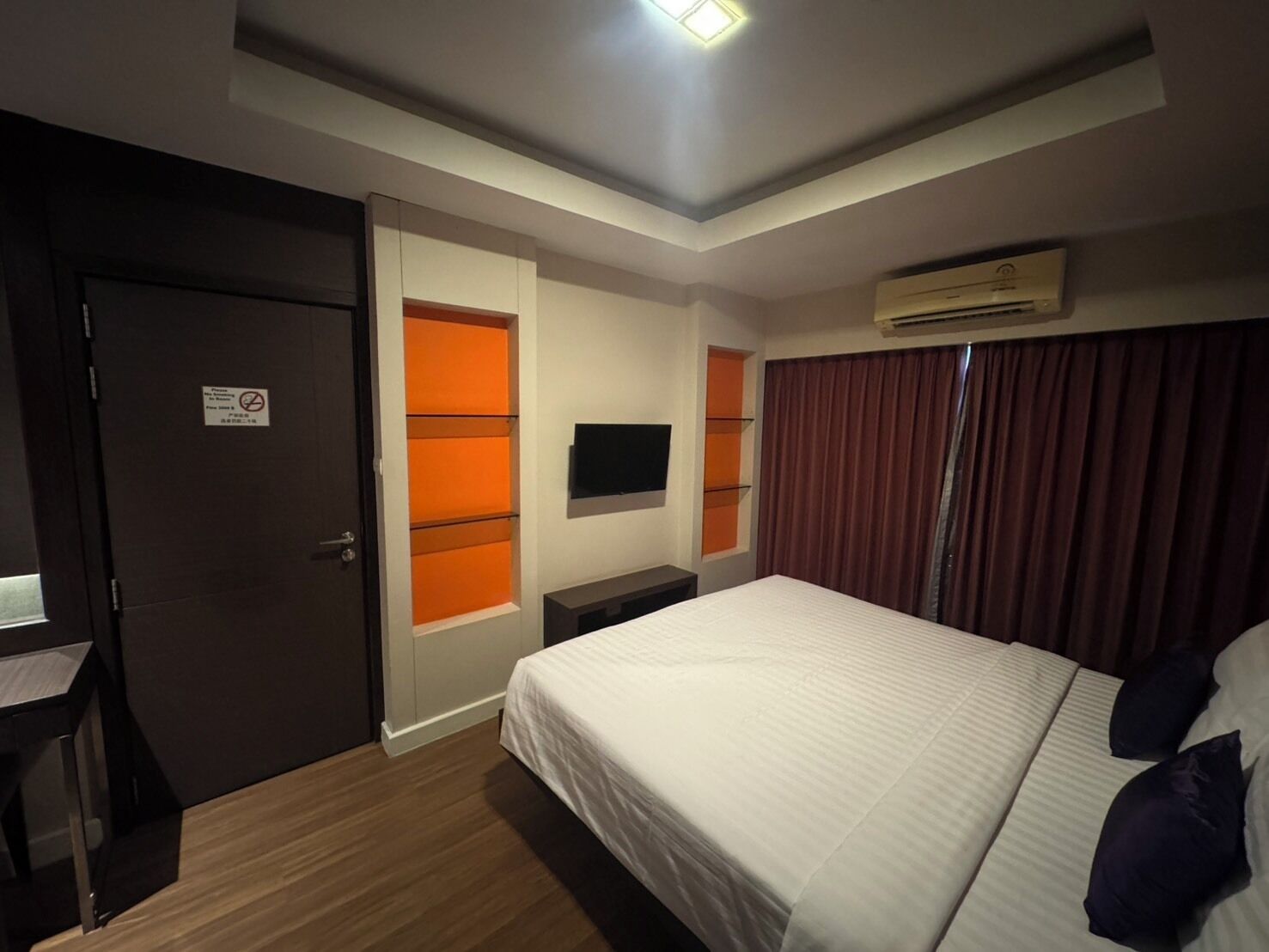A hotel room with a bed, a desk, a TV, and an air conditioning unit.
