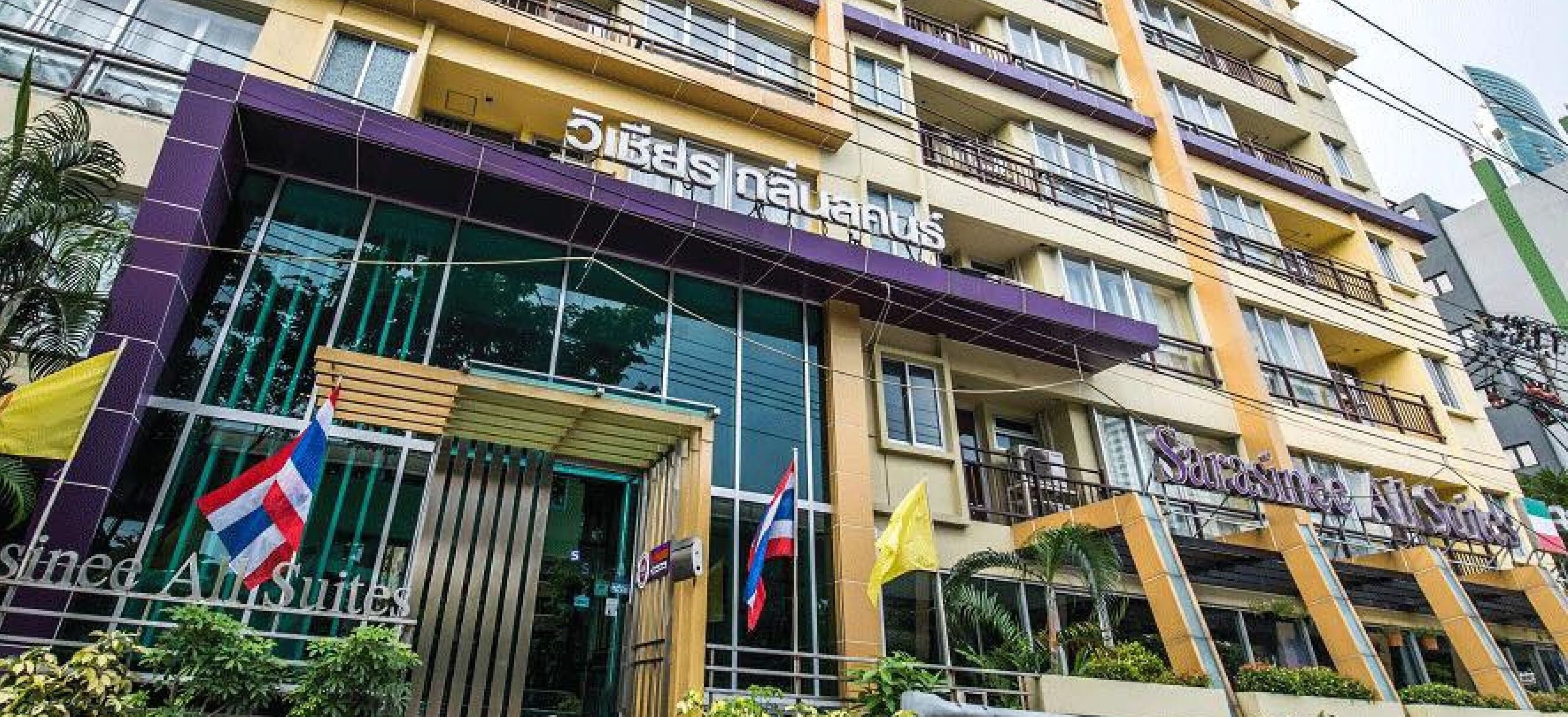 A hotel with multiple floors, balconies, and a prominent entrance with flags.